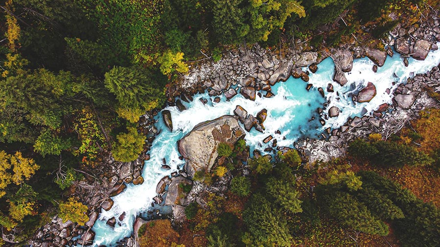 Vue aérienne d’une rivière incroyablement turquoise coulant au milieu d’un terrain rocheux, dans une forêt d’un vert luxuriant