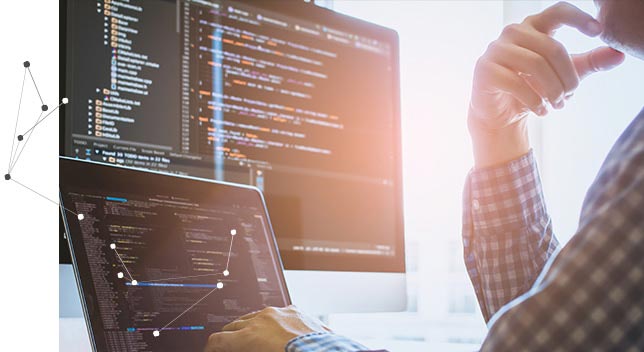 Un homme à un bureau tapant sur un clavier d’ordinateur portable et regardant un grand écran d’ordinateur affichant des lignes de données 