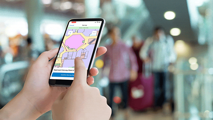 Mains tenant un téléphone mobile qui affiche une carte indoor en violet et rose d’un bâtiment public.