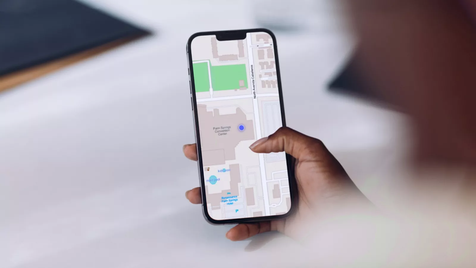 Main tenant un téléphone sur l’écran duquel est affichée une carte gris clair avec un marqueur bleu sur un arrière-plan flou