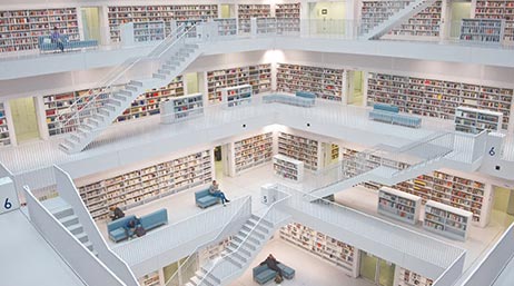 Vue intérieure d’une bibliothèque moderne de quatre étages dans des tons clairs avec un mobilier bleu élégant et de nombreuses étagères remplies de livres colorés