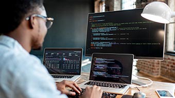 Homme à un bureau tapant sur un clavier et regardant un ordinateur portable et un grand écran d’ordinateur