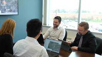 Quatre collaborateurs assis à une table dans une salle de conférence avec leur ordinateur portable près d’une grande fenêtre