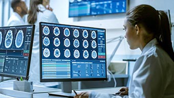 Professionnel de la santé en blouse blanche regardant des scintigraphies du cerveau sur un écran d’ordinateur