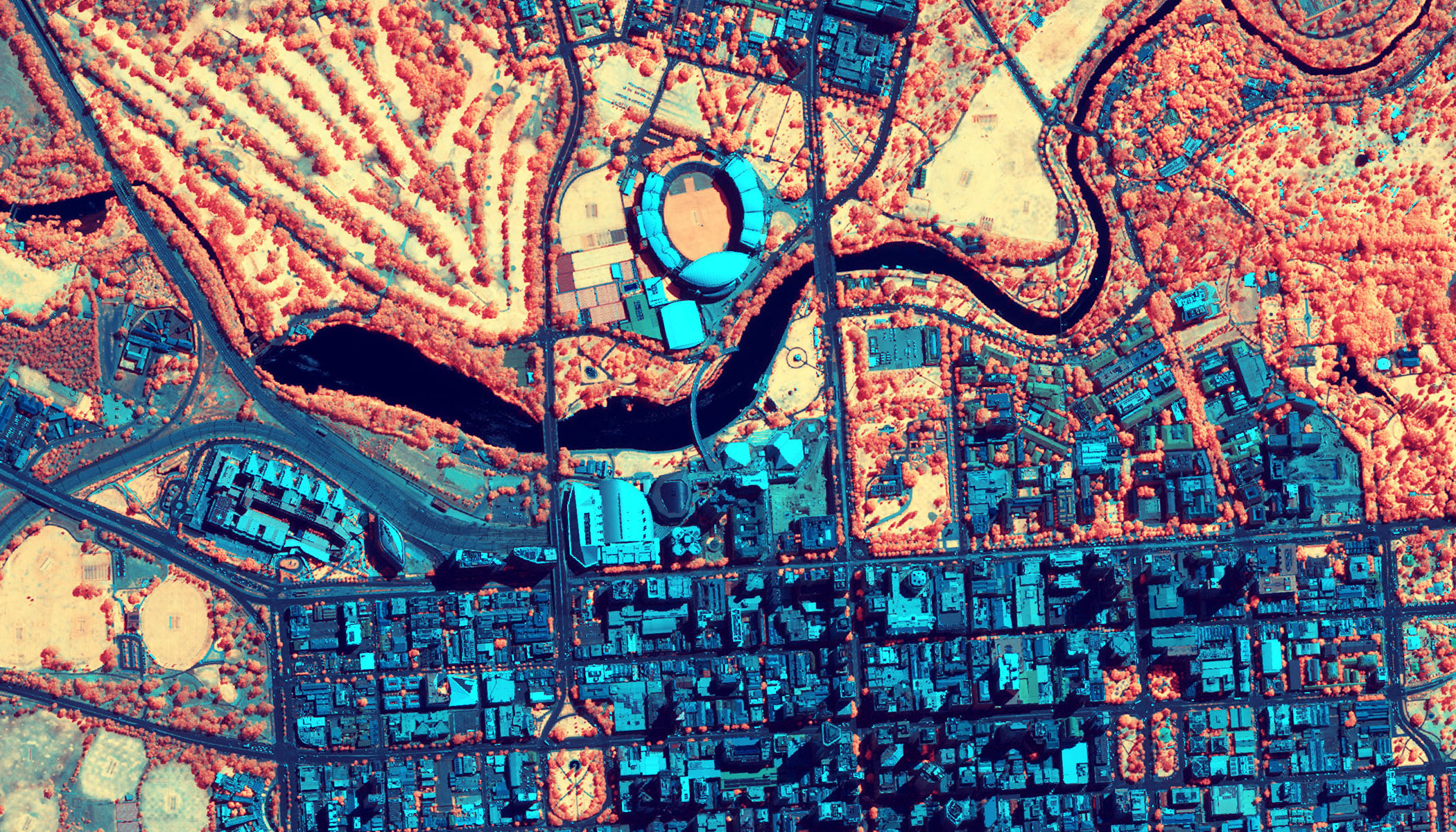 Carte satellite avec code couleur représentant une ville dans des tons de bleu, orange et rouge avec un fleuve, des espaces verts et une structure ressemblant à un stade sur un schéma urbain de type grille.
