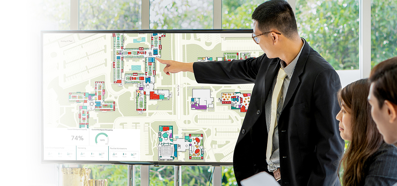 Cadre présentant à son équipe le plan d’un campus avec une interface d’aménagement de l’espace intérieur et un tableau de bord pour définir l’utilisation de l’espace