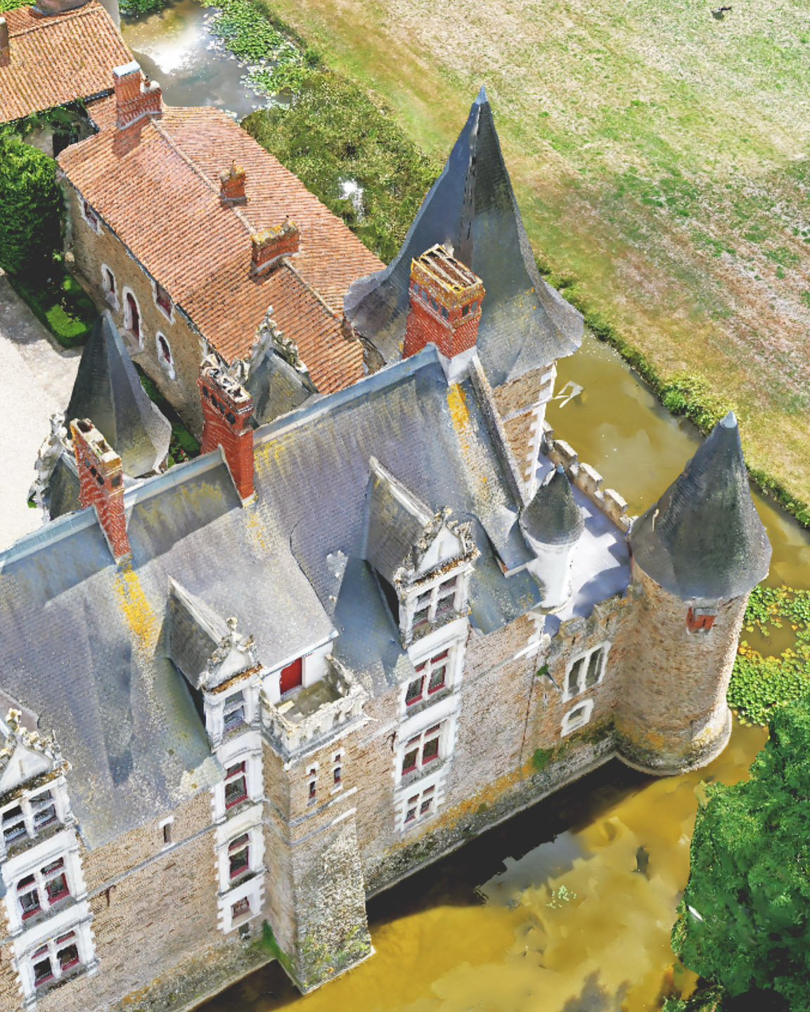 Image de drone hors nadir d’un pavillon ressemblant à un château avec une cour, entouré de douves et de vastes champs de terre agricole 