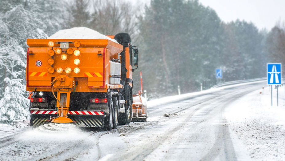 Chasse-neige orange descendant une route enneigée bordée d’arbres