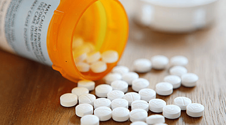 Boîte de médicaments orange renversée, d’où s’échappent de petits cachets blancs répandus sur une surface marron