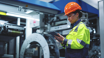 Femme portant un casque de sécurité et tenant une tablette à côté d’une machine imposante