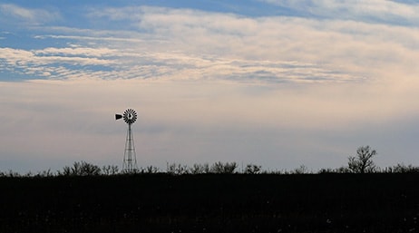 Photo d'une vaste plaine plate avec un moulin à vent dont la silouhette se découpe sur un ciel de crépuscule couvert en bleu pâle