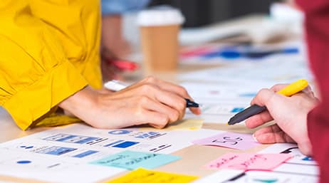 Gros plan des mains de deux personnes en train d’écrire avec un crayon et un marqueur sur des Post-it et des imprimés