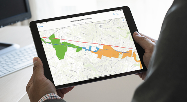 Personne tenant une tablette qui affiche une carte avec une zone en surbrillance orange, bleue et verte