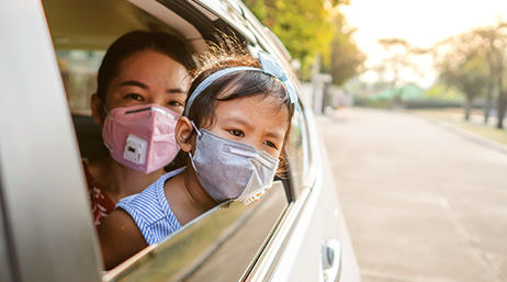 Femme portant un enfant dans une voiture, chacun portant un masque