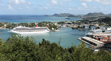 Rivage d’une ville côtière luxuriante avec des bateaux et des navires de croisière dans une marina, de vastes étendues d’eau au-delà et des collines vertes au loin