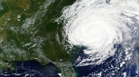 Image satellite d’un ouragan tourbillonnant au-dessus d’une masse continentale vert foncé et d’un océan bleu foncé.