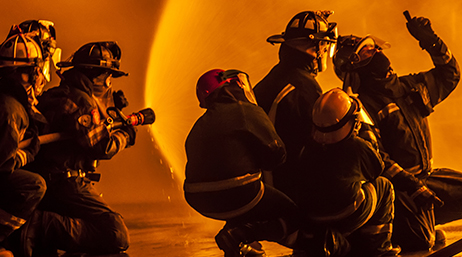 Photo dans une teinte orange de cinq sapeurs-pompiers pointant plusieurs tuyaux sur un brasier