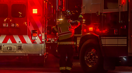 Premier intervenant se tenant à côté de deux voitures de pompier dans une rue la nuit dans une scène éclairée en rouge par les phares des camions
