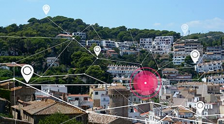 Image composite d’une banlieue de maisons couleur blanc et taupe nichées sur une colline verdoyante et boisée sous un ciel bleu clair recouvert par un réseau généré par ordinateur de lignes blanches et de points de carte connectés