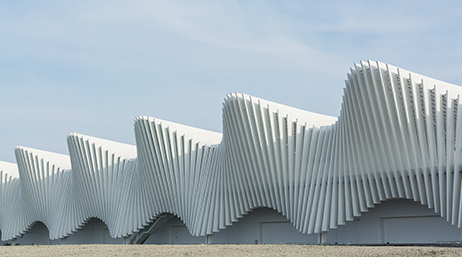 Le côté d’une gare moderne dont les murs ont la forme de vagues blanches massives sous un ciel bleu brumeux
