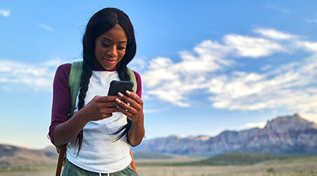 Personne portant un sac à dos et tenant un téléphone avec des montagnes en arrière-plan