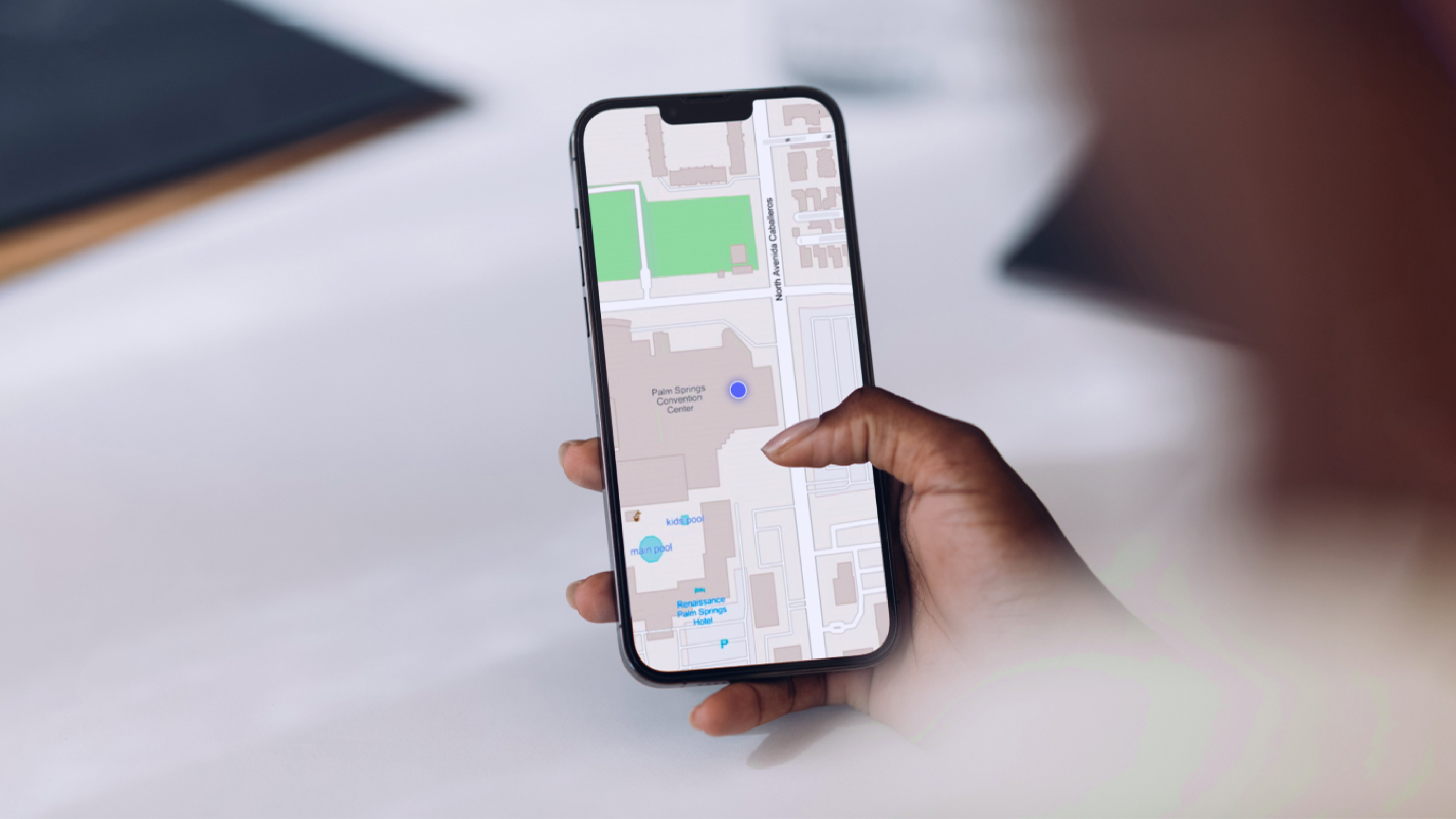 Main tenant un téléphone sur l’écran duquel est affichée une carte gris clair avec un marqueur bleu sur un arrière-plan flou