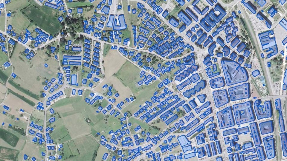 Vue aérienne de quartiers et de terres agricoles avec des bâtiments identifiés et délimités par un modèle d’IA