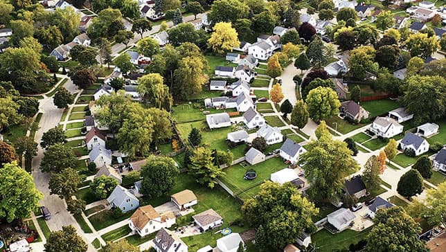 Image aérienne d’un lotissement arboré disposé le long d’allées incurvées avec de petites maisons blanches et des pelouses vertes