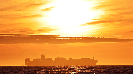 Grand navire transportant des conteneurs voyageant à l'horizon sous un soleil couchant